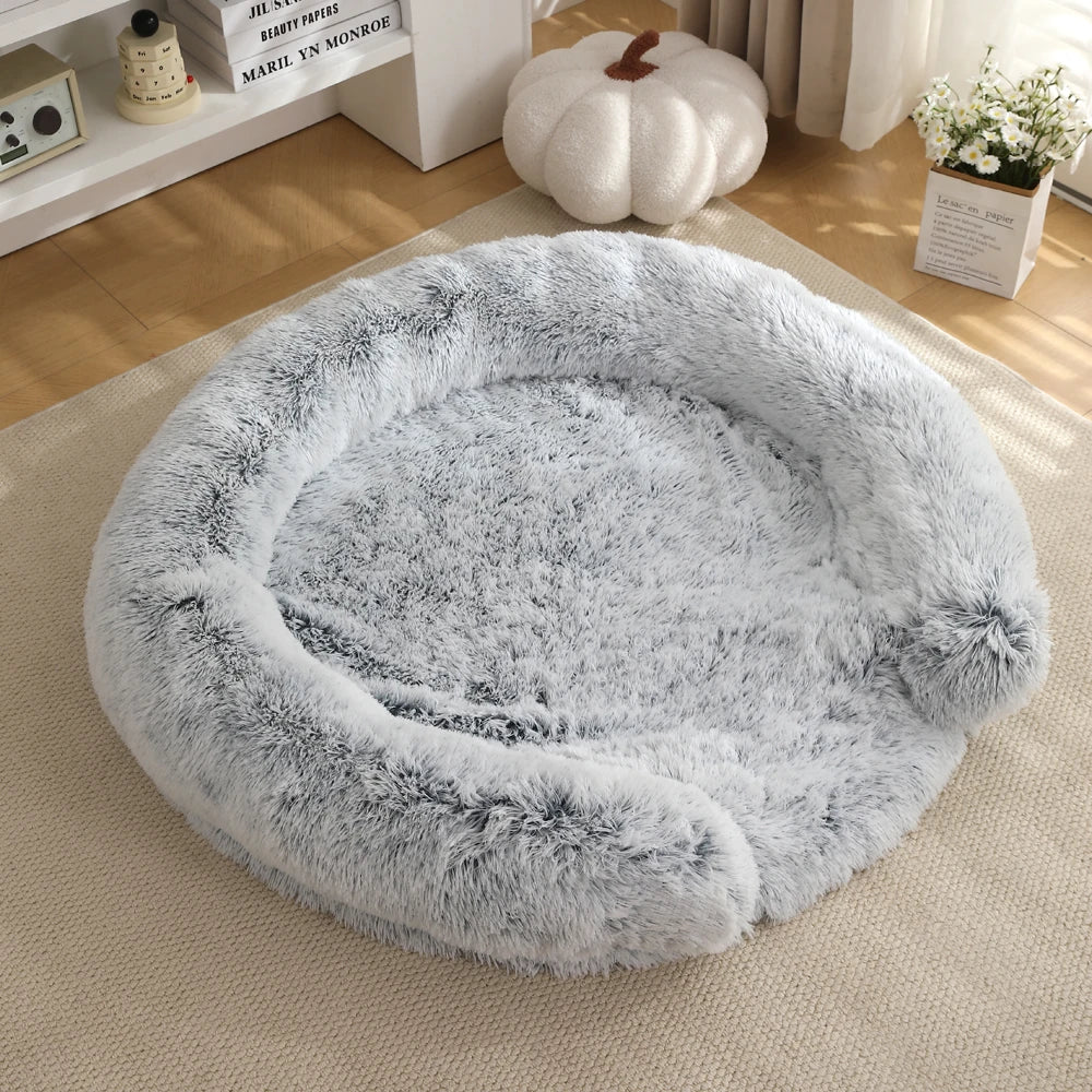 A round, fluffy gray dog bed with a removable cover resting on a light beige rug.