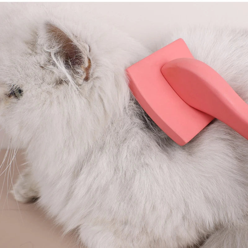 A white cat is being groomed with a pink ergonomic pet grooming rake featuring stainless steel teeth.