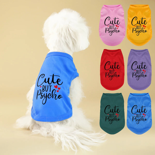 A white fluffy dog is wearing a blue vest with the text Cute but Psycho and several other colored vests.