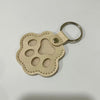 A light beige leather pet fur keepsake keychain charm with a rounded shape and a metal ring.