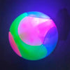A glowing rubber fetch ball for dogs, illuminated with vibrant pink, green, and blue light.