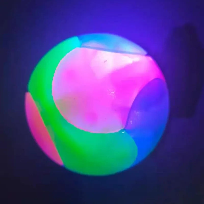 A glowing rubber fetch ball for dogs, illuminated with vibrant pink, green, and blue light.