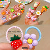 Assortment of cute cartoon elastic hair ties featuring various fruit and flower designs on a hand