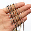 A hand holds a set of gold and silver plated ball necklaces with various bead colors.