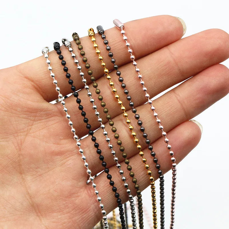 A hand holds a set of gold and silver plated ball necklaces with various bead colors.