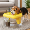 A yellow pet drinking fountain with a water flow mechanism is placed on a glass base on a light-colored rug.