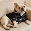 Ein hellfarbiger Französische Bulldogge trägt ein schwarzes Satin-Pyjama-Oberteil mit weißer Borte und ein passendes Schleife