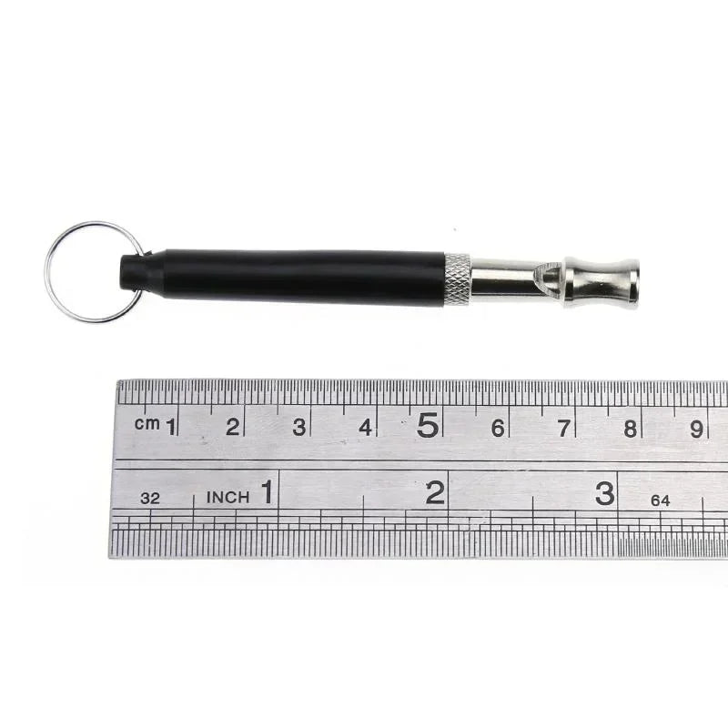 Black ultrasonic dog training whistle with a metal tip shown next to a ruler.