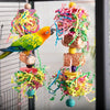 A vibrant orange and green parrot is perched on a wooden toy that shreds colorful paper and string.