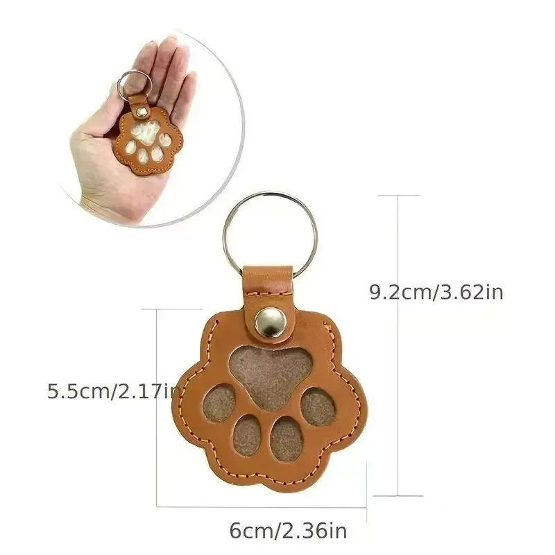 A brown leather pet paw print keepsake with a metal loop and a textured surface.