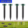 Four black solar ultrasonic pest repellers inserted into the ground on a green lawn.