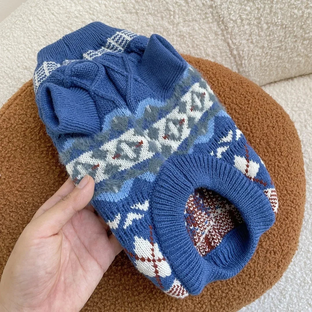 A hand holds a blue knit pet sweater for dogs and cats with white and gray patterned details.