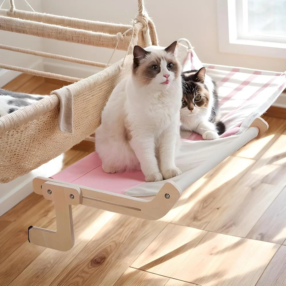 A fluffy white and gray cat is resting on a light wood window perch with a pink cushion.