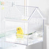 A clear plastic house-style feeder for a small yellow bird, placed inside a wire cage.