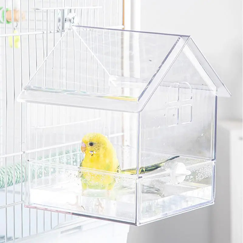A clear plastic house-style feeder for a small yellow bird, placed inside a wire cage.