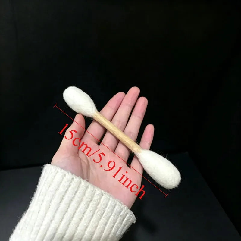 Una mano sostiene un juguete de hisopo de manzanilla blanco y esponjoso, de 15 cm de largo.