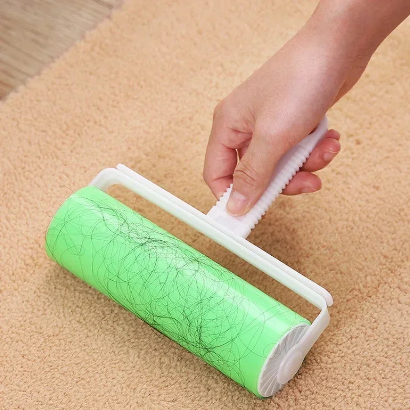 A hand is using a white lint roller to remove pet hair from a green roll on a beige carpet.