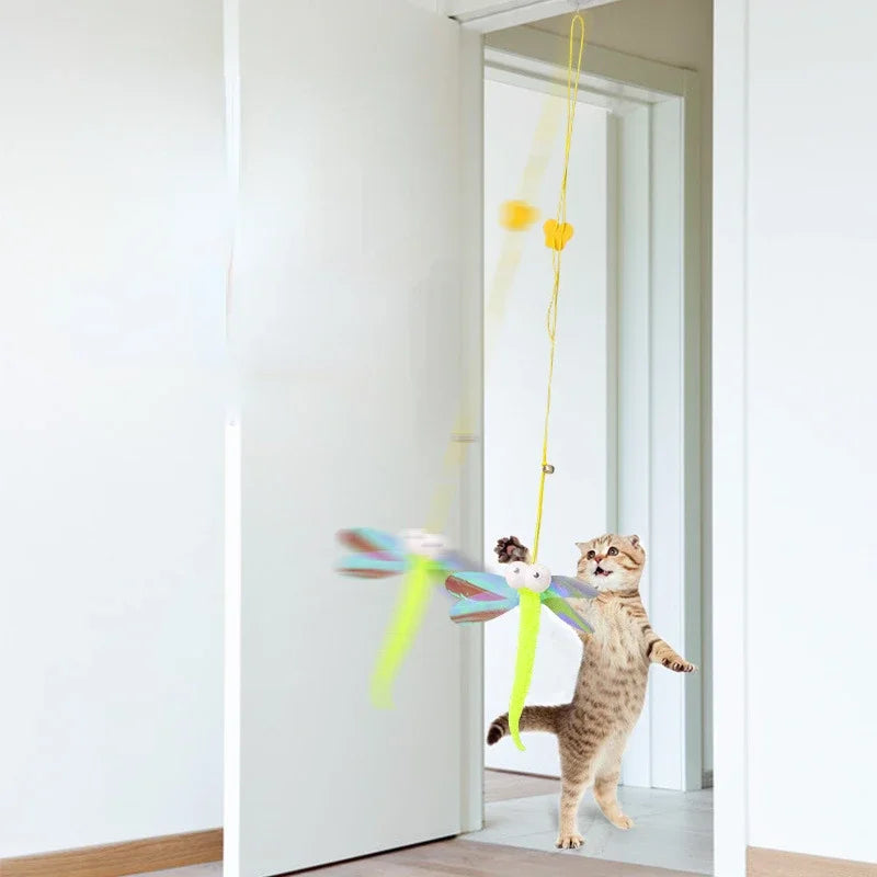 A tabby cat is playing with an interactive hanging toy featuring a colorful ribbon and adjustable rope inside a white room.