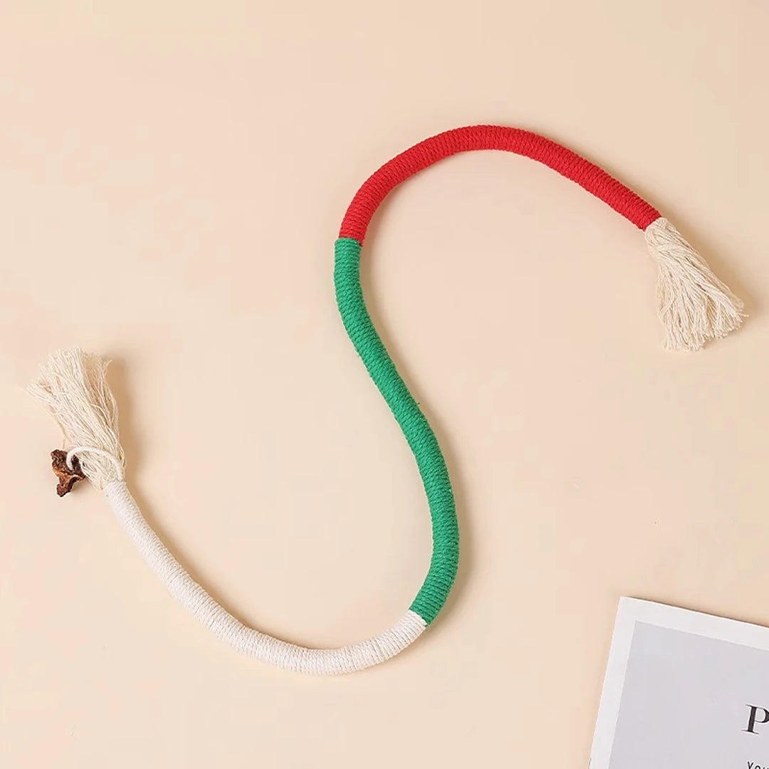 A curved rope toy with red and green sections and fluffy ends is displayed on a light background.