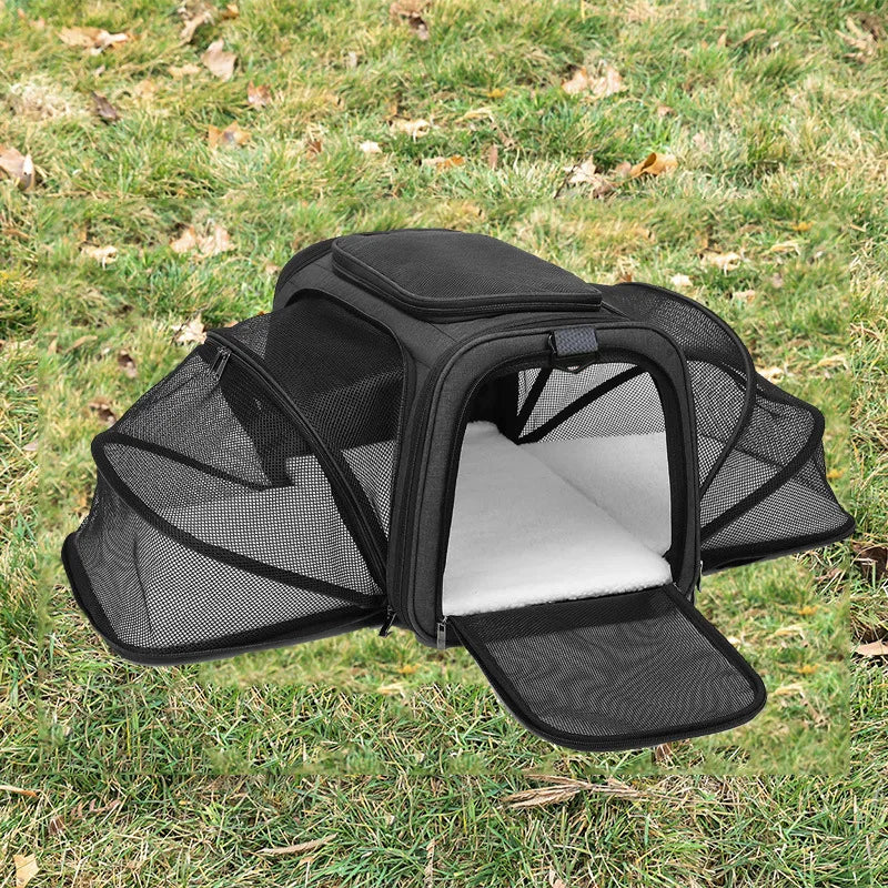 A black foldable soft-sided pet carrier is shown open on green grass.