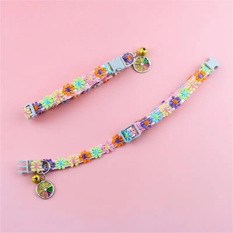 A colorful rainbow flower cat collar with a bell displayed on a pink background.
