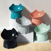 A collection of five elevated cat bowls in various shades of teal, pink, gray, and black, displayed on a light wooden surface