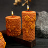 An orange honeycomb silicone mold for candles is shown with a lit candle and a golden flower decoration.