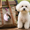 A fluffy white dog sits next to a tan bag with a pink stainless steel water dispenser attached.