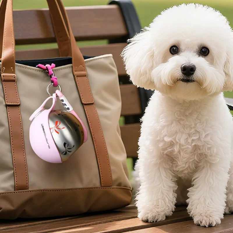 A fluffy white dog sits next to a tan bag with a pink stainless steel water dispenser attached.