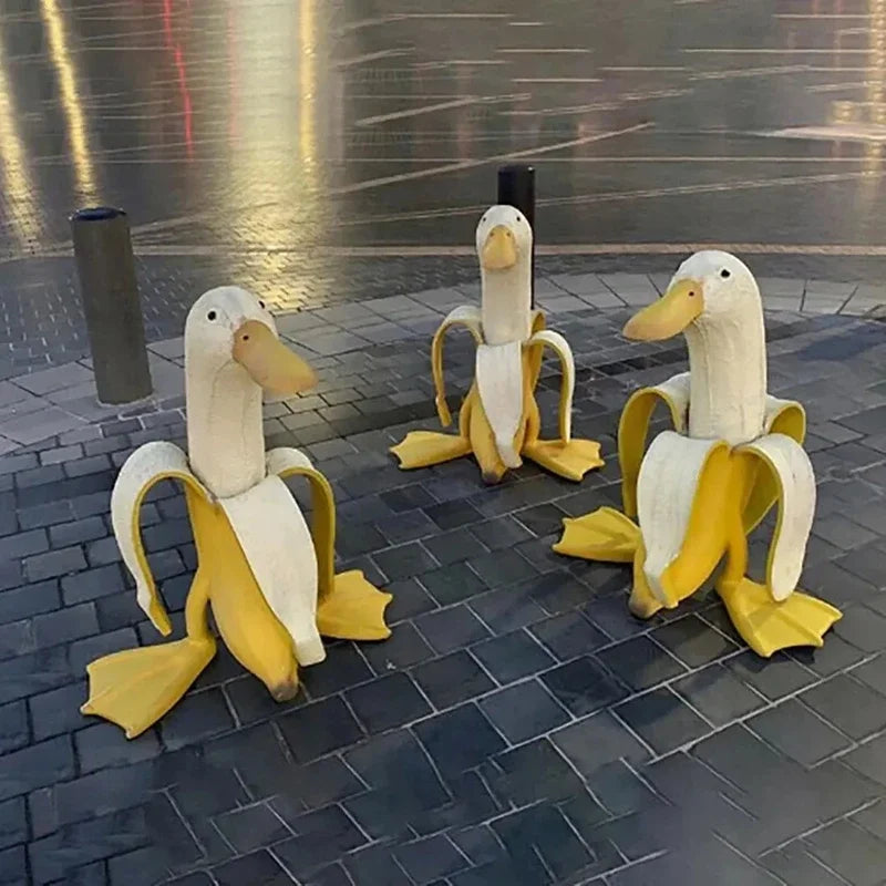 Skulptur einer weißen Ente mit gelben Akzenten, die eine Bananenförmige ähnelt, auf einer dunklen Fliesenoberfläche.