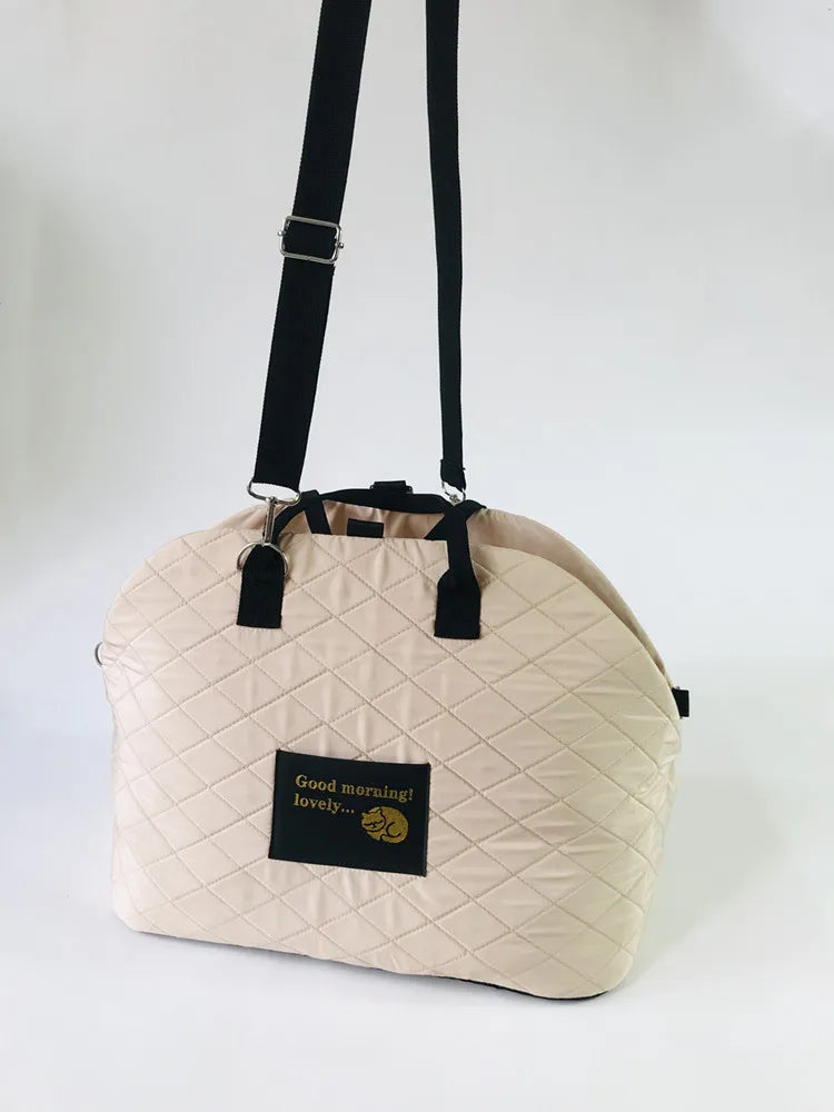 A beige soft-sided pet carrier with black straps and a small tag reading Good morning lovely