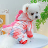 A white fluffy dog wearing pink and blue tie-dye fleece overalls.