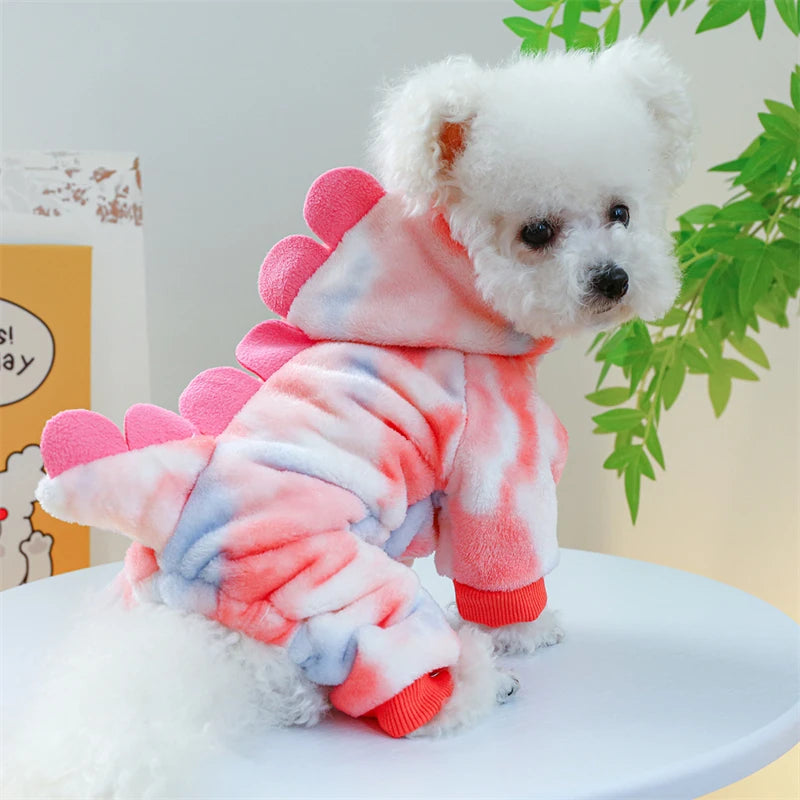 A white fluffy dog wearing pink and blue tie-dye fleece overalls.