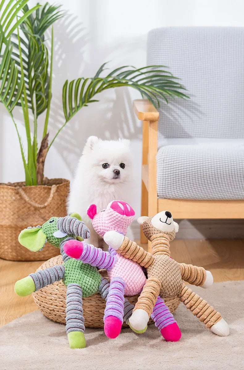 Ein weißer flauschiger Hundespspielzeug sitzt auf einem beige Teppich neben einer Zimmerpflanze und einem Holzstuhl.