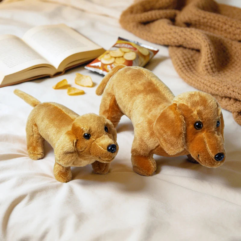 A tan plush dachshund toy lying on a light fabric next to a book and some dog treats.