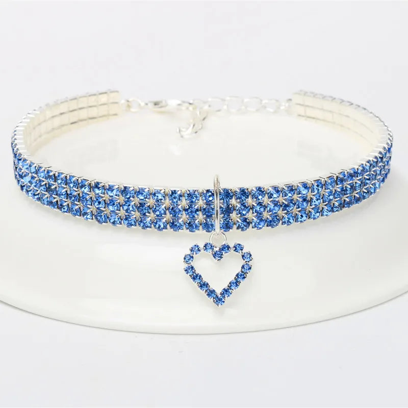 A sparkling blue rhinestone collar with a heart pendant, displayed on a white background.