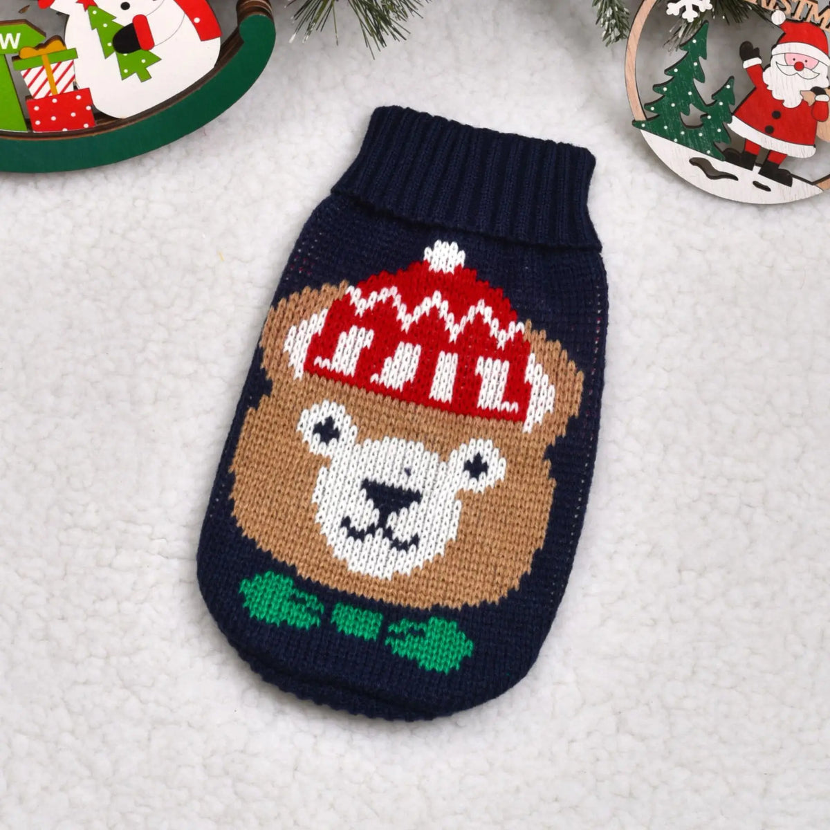 A knitted winter dog sweater featuring a brown bear face with a red hat and green collar.