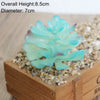 A light blue artificial succulent plant with a round, layered form is displayed in a wooden box surrounded by small pebbles.