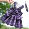 A purple and gray plaid reusable dog harness dress with a bow and attached clip.