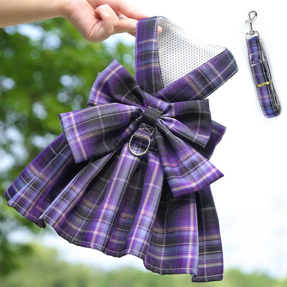 A purple and gray plaid reusable dog harness dress with a bow and attached clip.