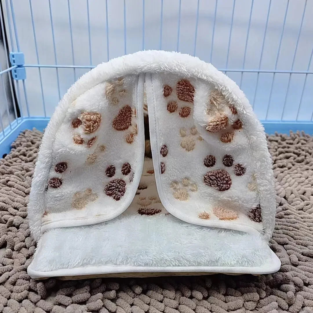 Hamaca de mascota blanca y esponjosa con huellas de pata marrones, exhibida sobre una superficie gris texturizada.