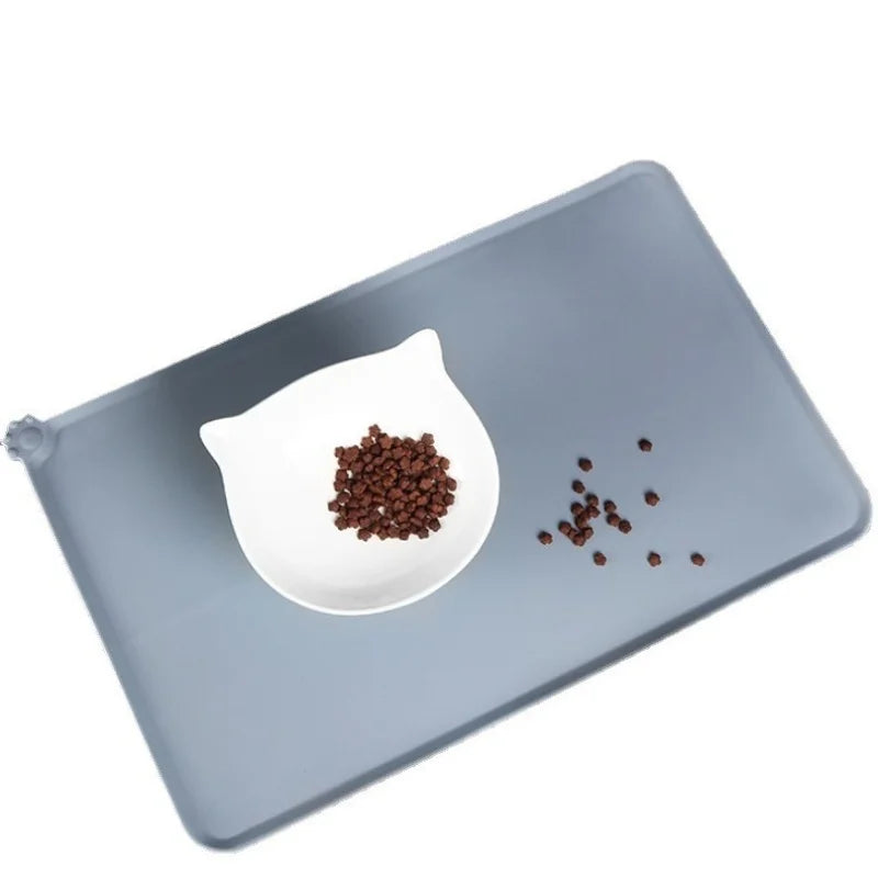 A gray silicone pet feeding mat with a white bowl containing dark brown kibble.