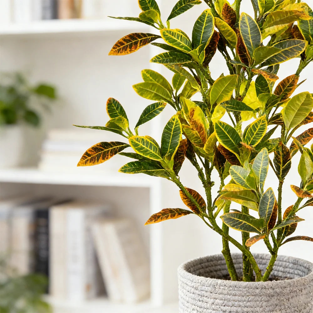 Artificial croton tree with vibrant green and orange tropical leaves potted in a gray fabric planter