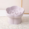 A white ceramic slow feeder bowl for pets featuring a flower design, placed on a striped mat.