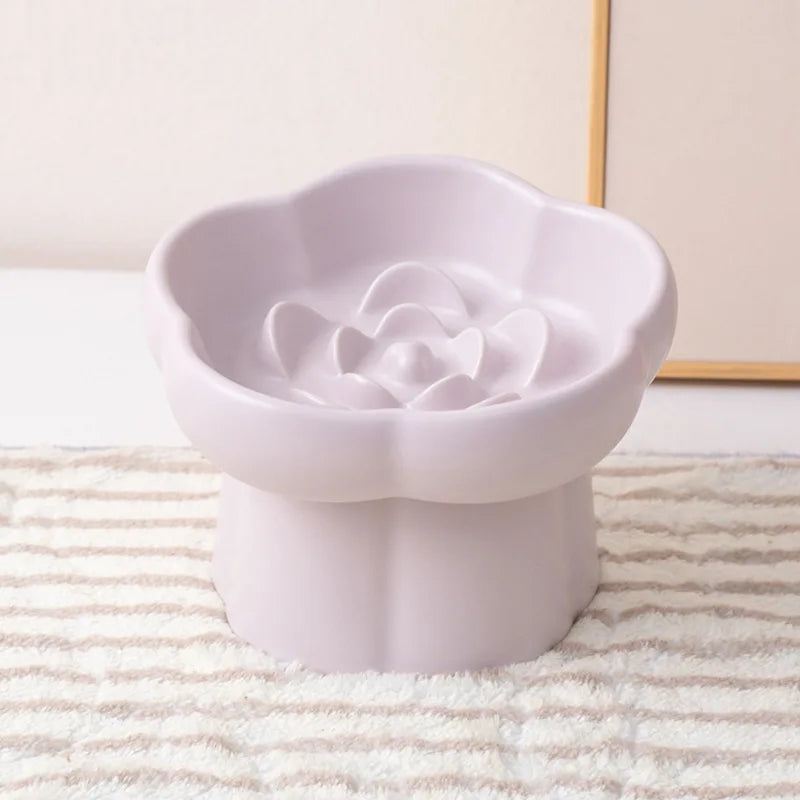 A white ceramic slow feeder bowl for pets featuring a flower design, placed on a striped mat.