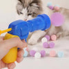 A cat is playing with a blue plush ball launcher, surrounded by colorful soft balls.