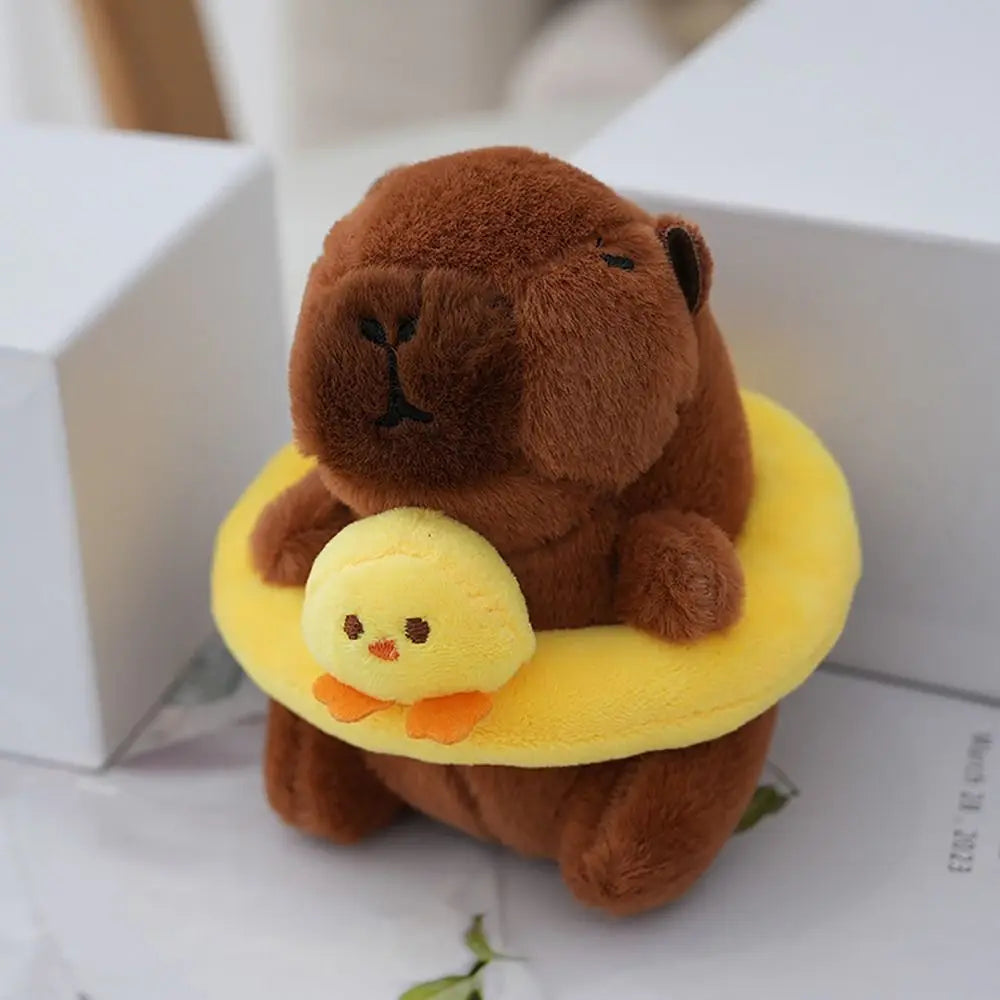 Braune Capybara-Plüschpuppe mit gelbem Hoodie und einem kleinen gelben Küken auf einer weißen Box.
