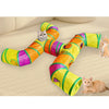 A colorful, striped rainbow cat tunnel is stretched out on a light carpet with several cats interacting with it.