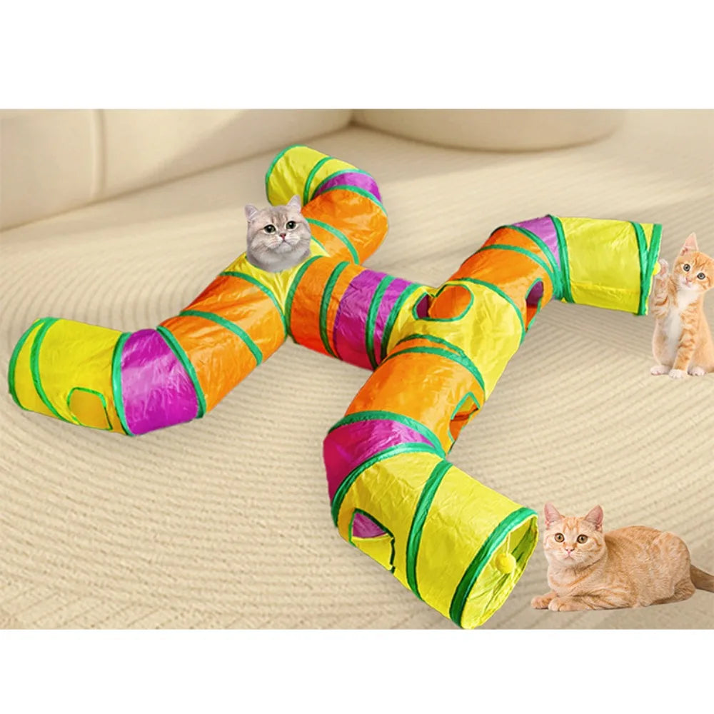 A colorful, striped rainbow cat tunnel is stretched out on a light carpet with several cats interacting with it.