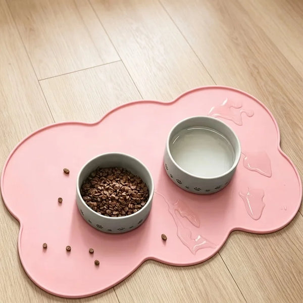 A pink silicone pet placemat with raised edges holds a small bowl of dry food and a separate white bowl.
